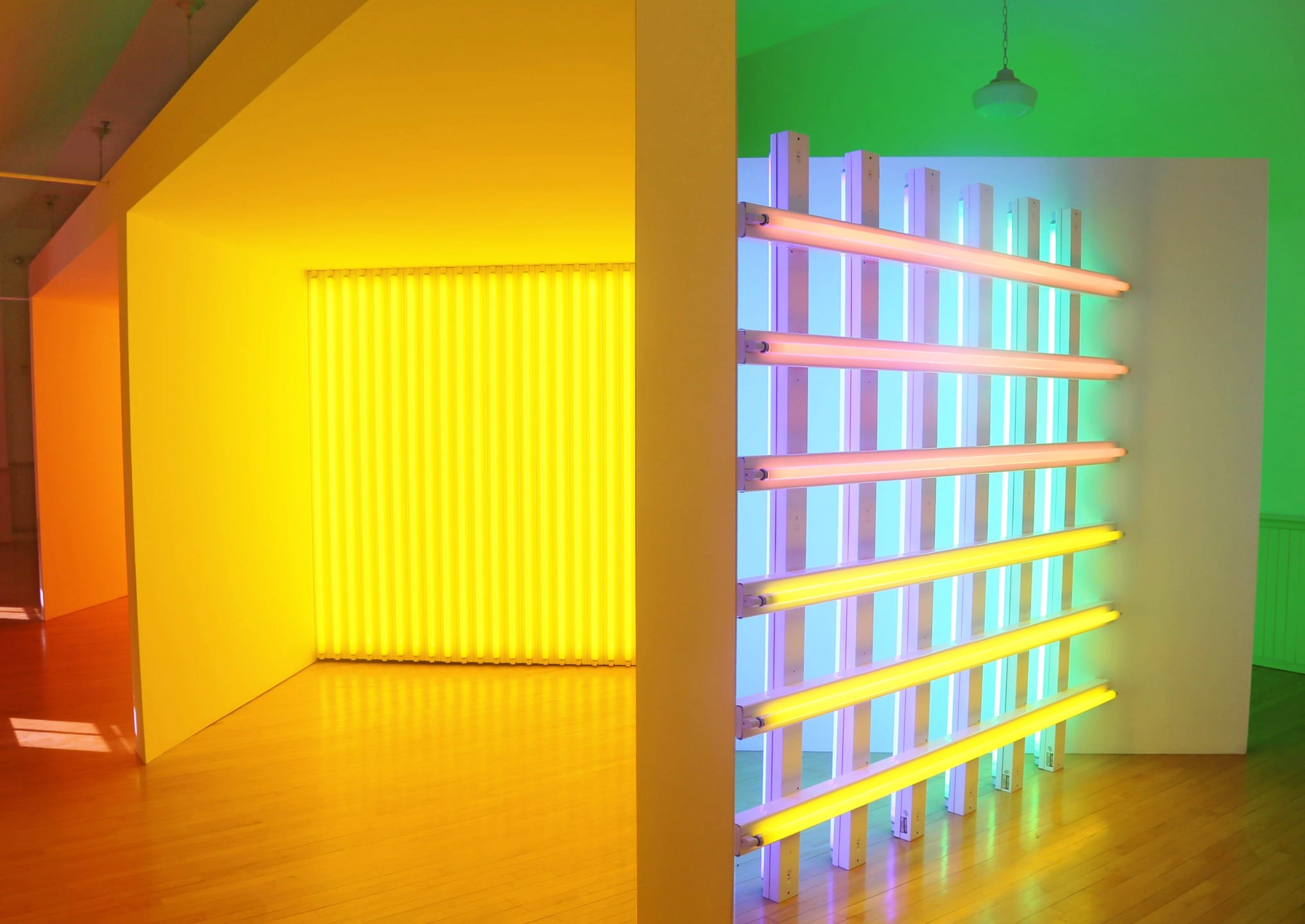 Colorful art installation with vibrant neon lights in yellow, blue, and green, illuminating a modern room with wooden floor.