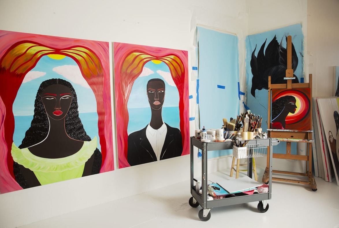 Art studio with two portraits on the wall, an easel with a painting, and a cart holding art supplies.