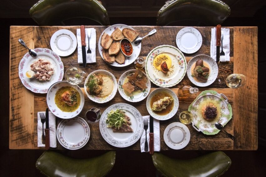 Top view of a wooden table set with various Middle Eastern dishes, including appetizers and bread, surrounded by chairs.