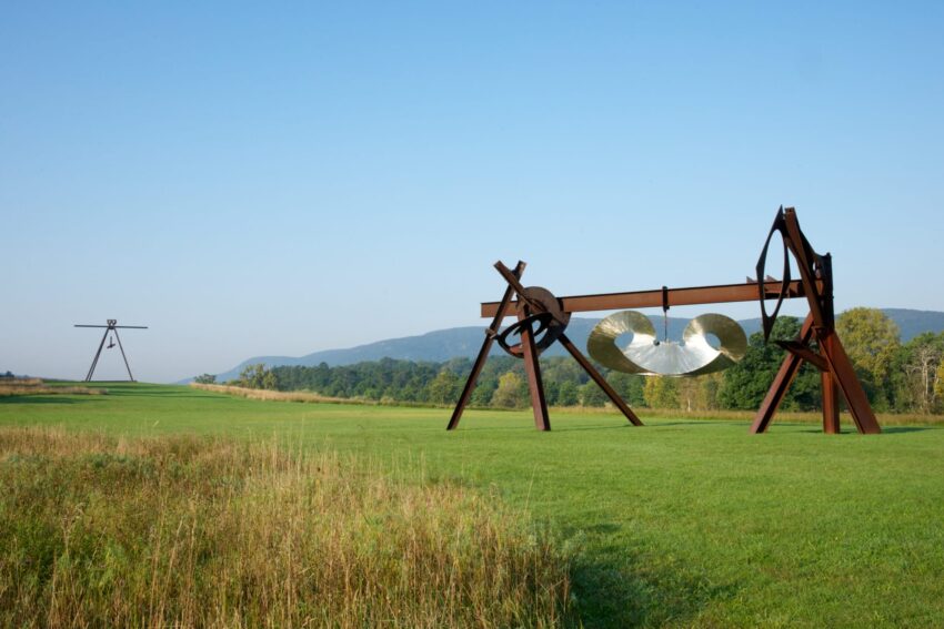 Large outdoor metal sculptures on grassy field with distant hills and clear blue sky.