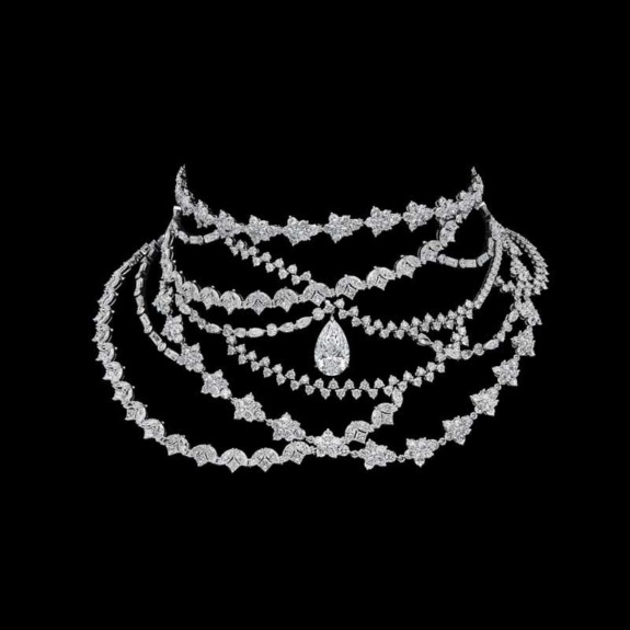 Intricate diamond necklace with multiple layers and a teardrop pendant against a black background.