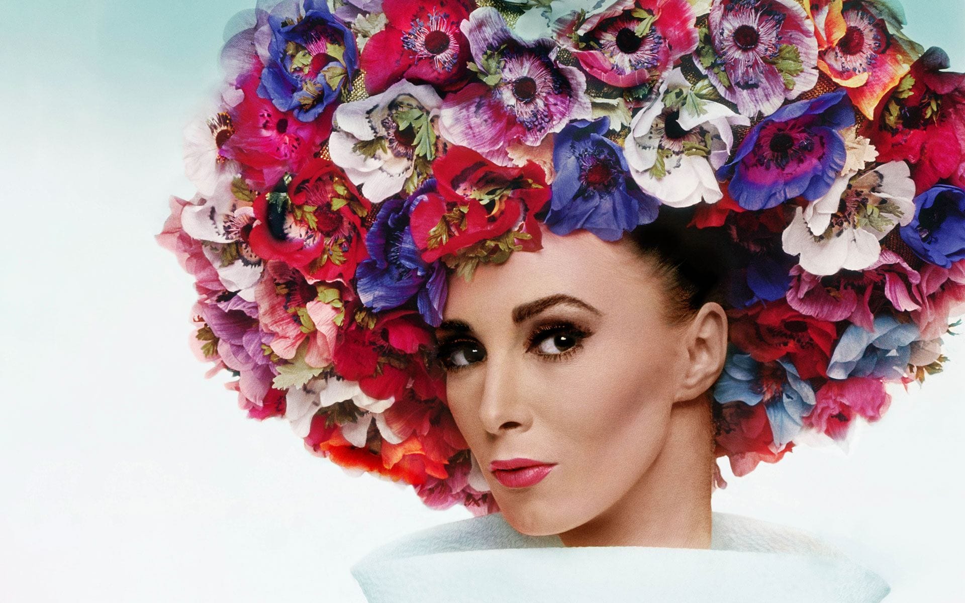 Woman with vibrant floral headpiece and elegant makeup against a soft background