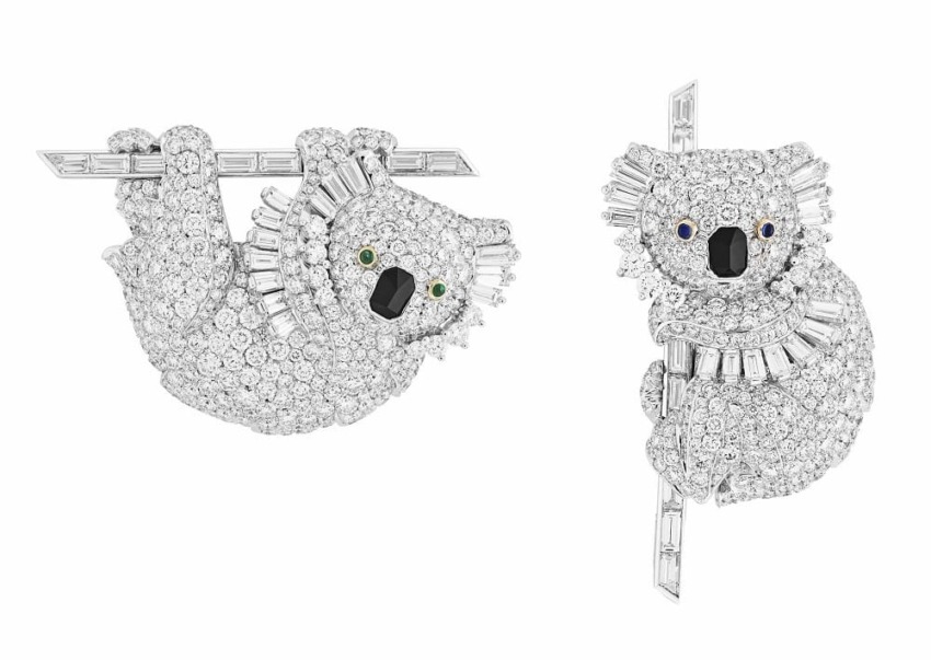 Two koala bear brooches encrusted with shiny diamonds and gemstones, hanging onto small branches.