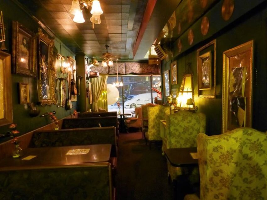 Cozy vintage-style restaurant with dim lighting, ornate mirrors, floral wallpaper, and antique decorations.