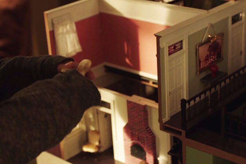 Person arranging a dollhouse with a visible pink room, fireplace, and painting labeled "GIRL" on the wall.
