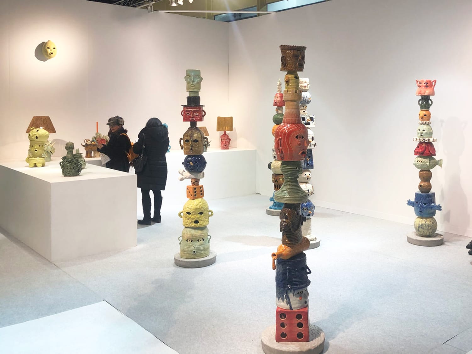 Exhibit showcasing colorful ceramic sculptures of stacked, whimsical faces in an art gallery setting.