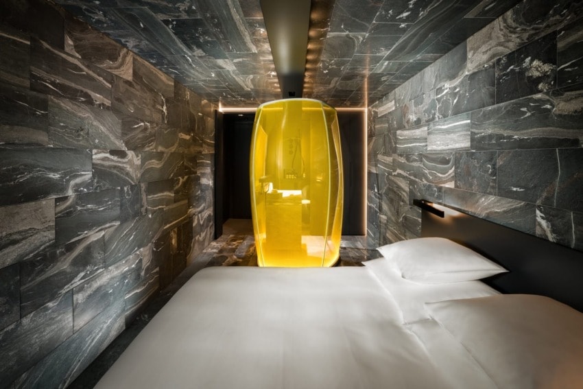 Modern hotel room with marble walls, a sleek bed, and a unique yellow glass centerpiece in the center.