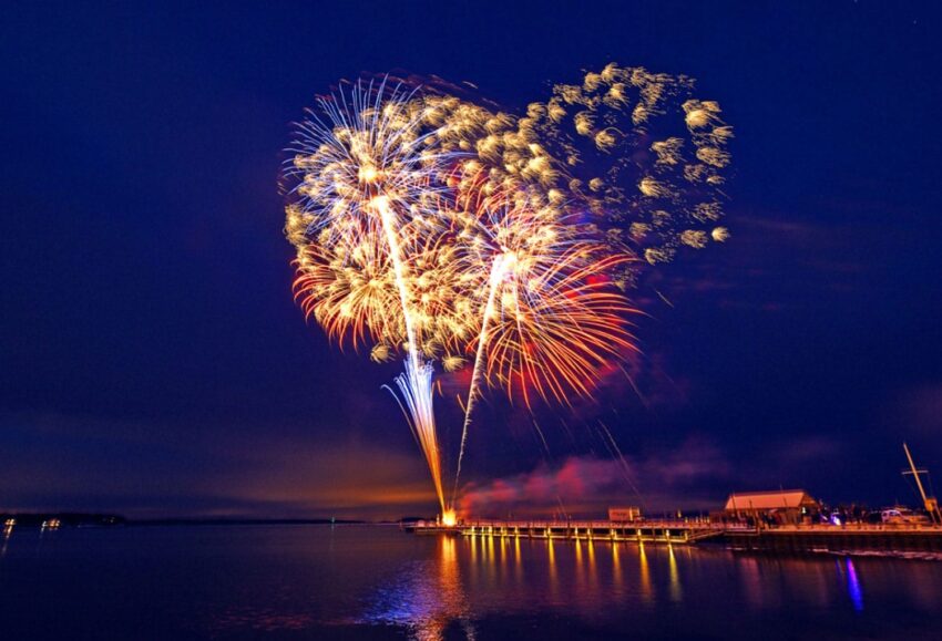 Colorful fireworks exploding over a calm lake at night, lighting up the sky with vibrant patterns and reflections on the water.