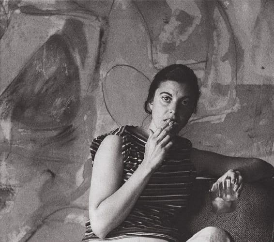 Person seated, holding a drink, and eating, with an abstract wall painting in the background.