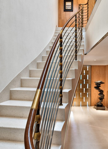 Elegant curved staircase with wooden handrail and modern sculpture, leading up to a bright hallway with wall decor.