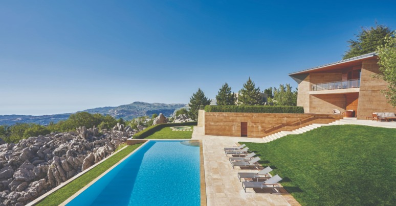Luxury hillside villa with infinity pool, sun loungers, and scenic mountain views under a clear blue sky.