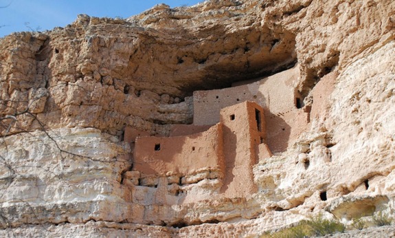 Ancient cliff dwellings built into rugged sandstone cliffs beneath a clear blue sky.