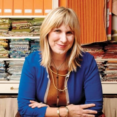 Person smiling in front of colorful fabric stacks on shelves
