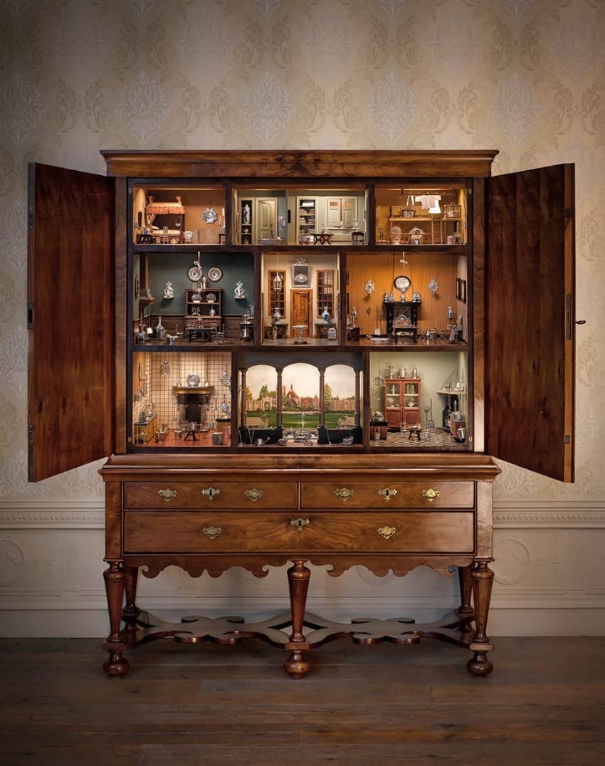 Antique wooden cabinet with miniature dollhouse rooms displayed inside, showcasing detailed interior decor and furniture.