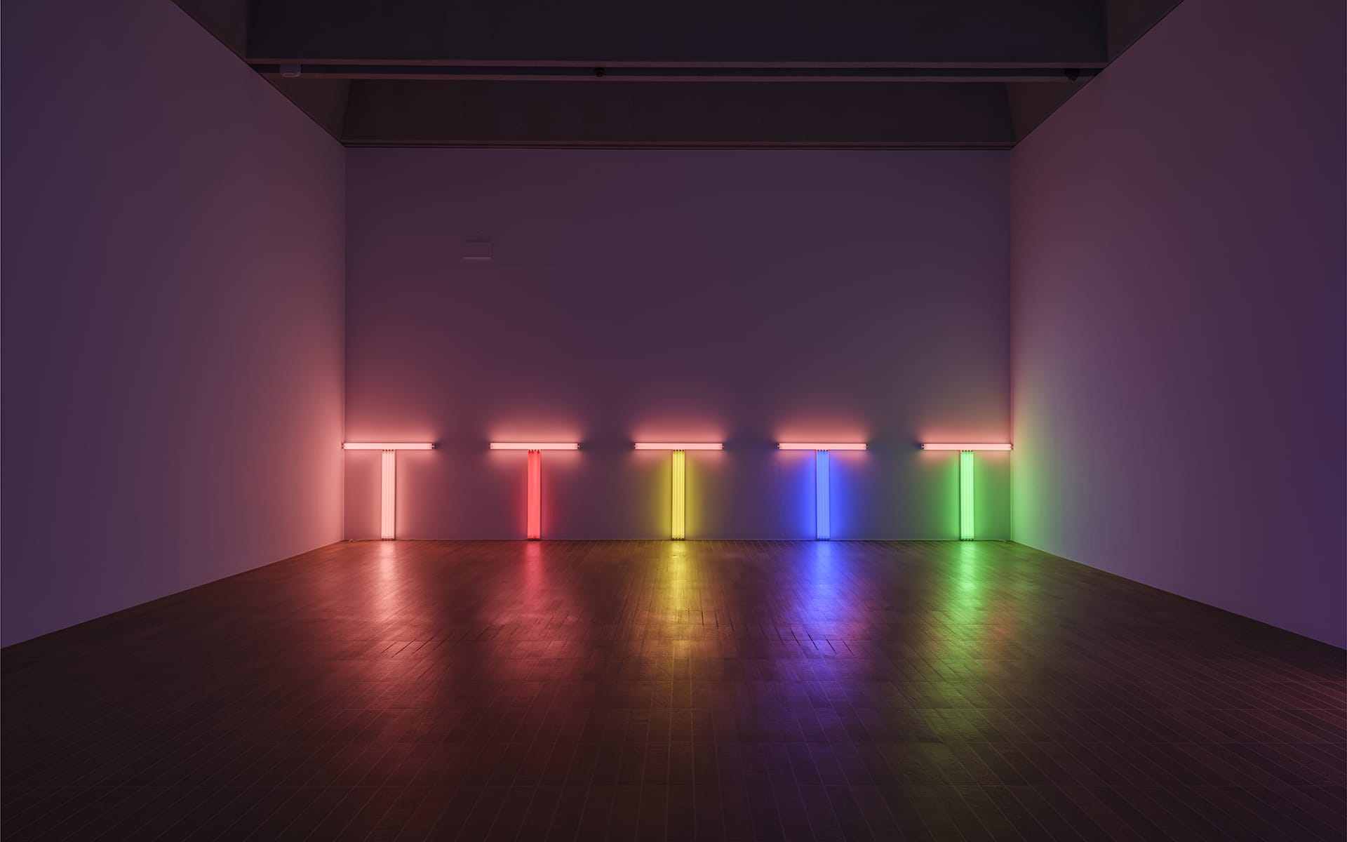 A minimalist room with a neon art installation displaying vertical lines in red, orange, yellow, green, and blue on the wall.