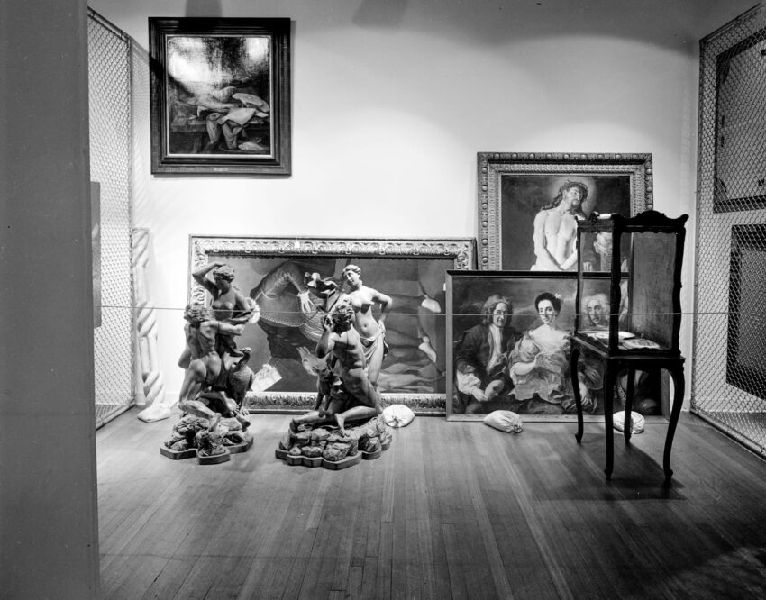 Art gallery display with classical sculptures, framed paintings, and an antique chair in a neatly arranged exhibition space.