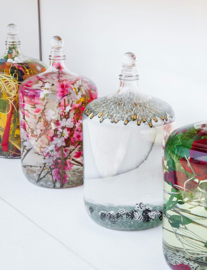 Glass jars filled with colorful floral arrangements and decorative elements on a white surface.