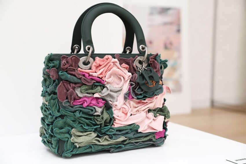 Elegant handbag with textured, colorful fabric ruffles in green, pink, and purple shades, displayed on a table.