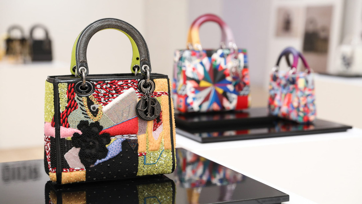 Colorful designer handbags displayed in an art gallery setting with focus on a front bag featuring a textured patchwork design.