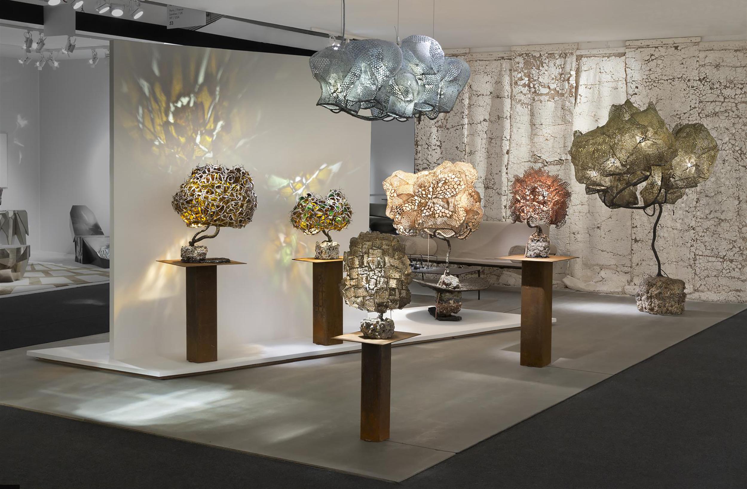Exhibit of uniquely sculpted lamps on stands casting intricate shadows in a modern gallery setting.
