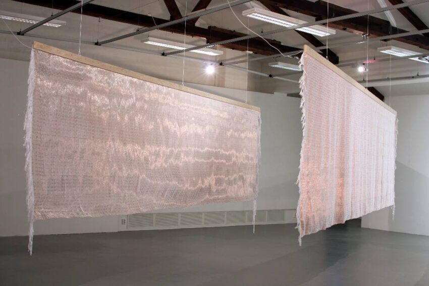 Two large, translucent fabric panels hanging in a gallery with exposed beams and modern lighting in the background.