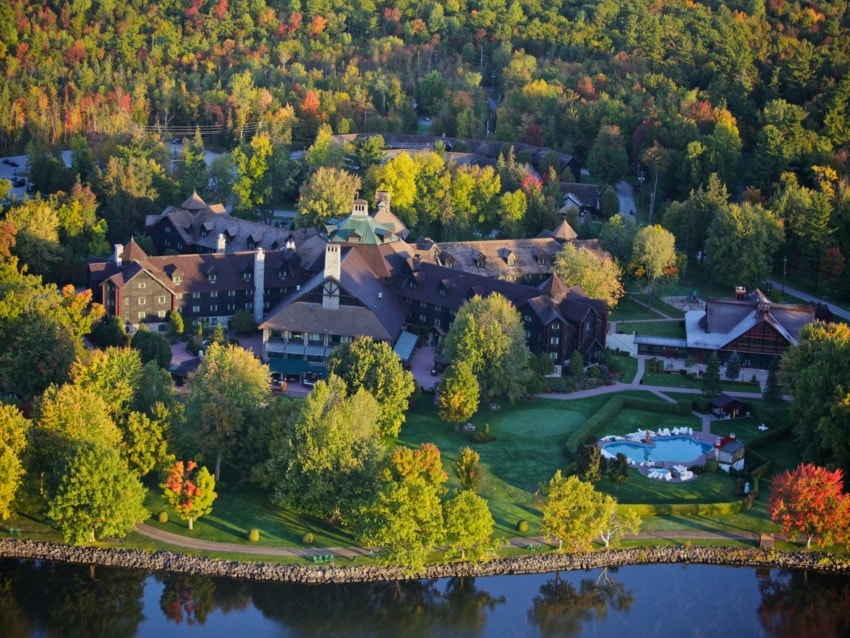 Aerial view of a large lodge surrounded by colorful autumn trees near a reflective lake.