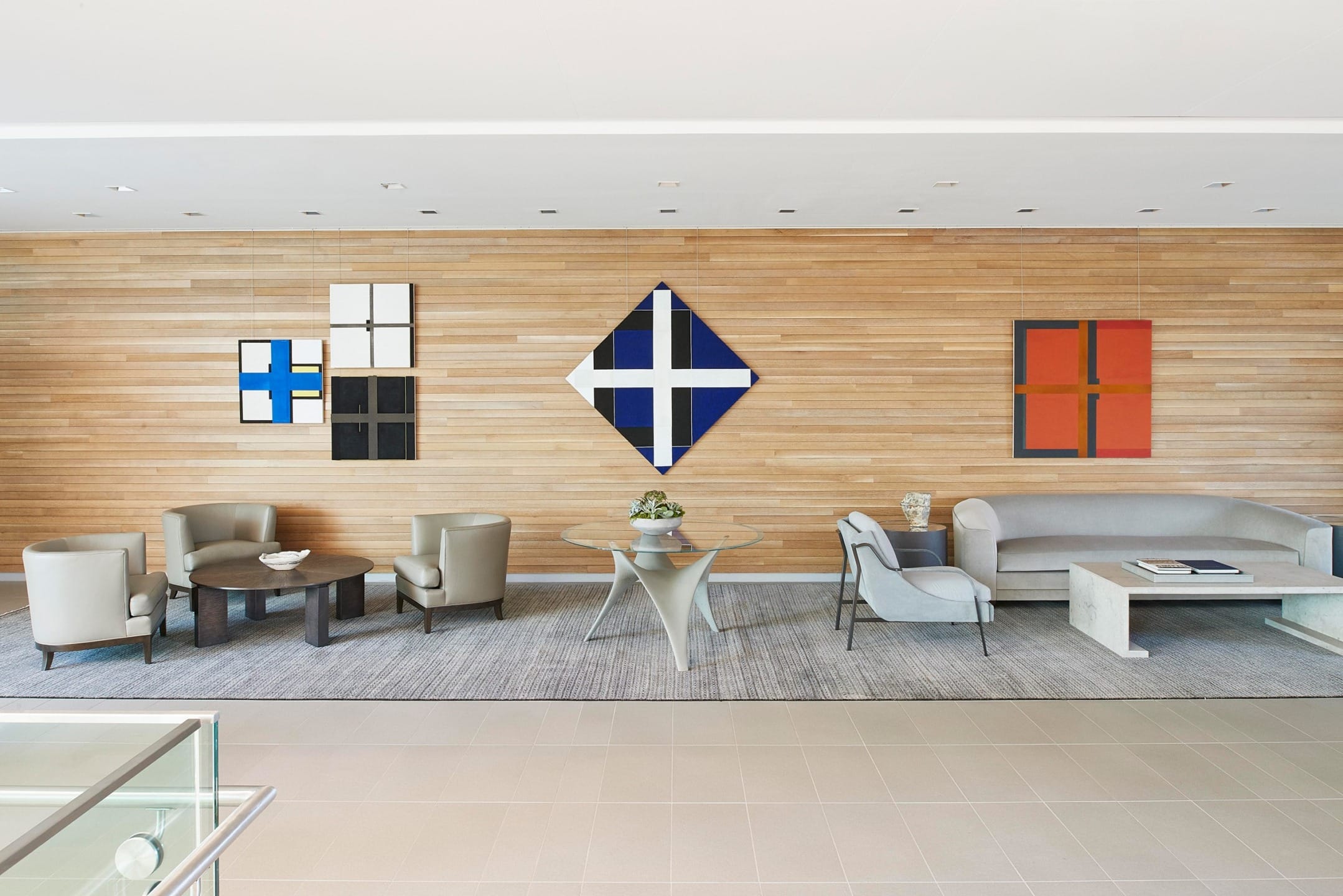 Modern lounge area with gray chairs, sleek tables, and colorful geometric artwork on a wood-paneled wall.