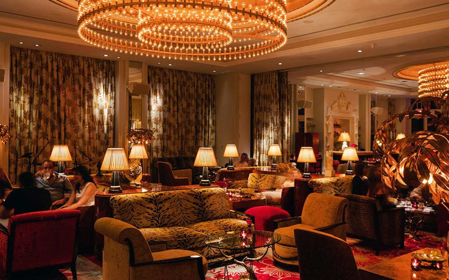 Elegant hotel lounge with plush seating, warm lighting, chandeliers, and guests enjoying a cozy atmosphere.