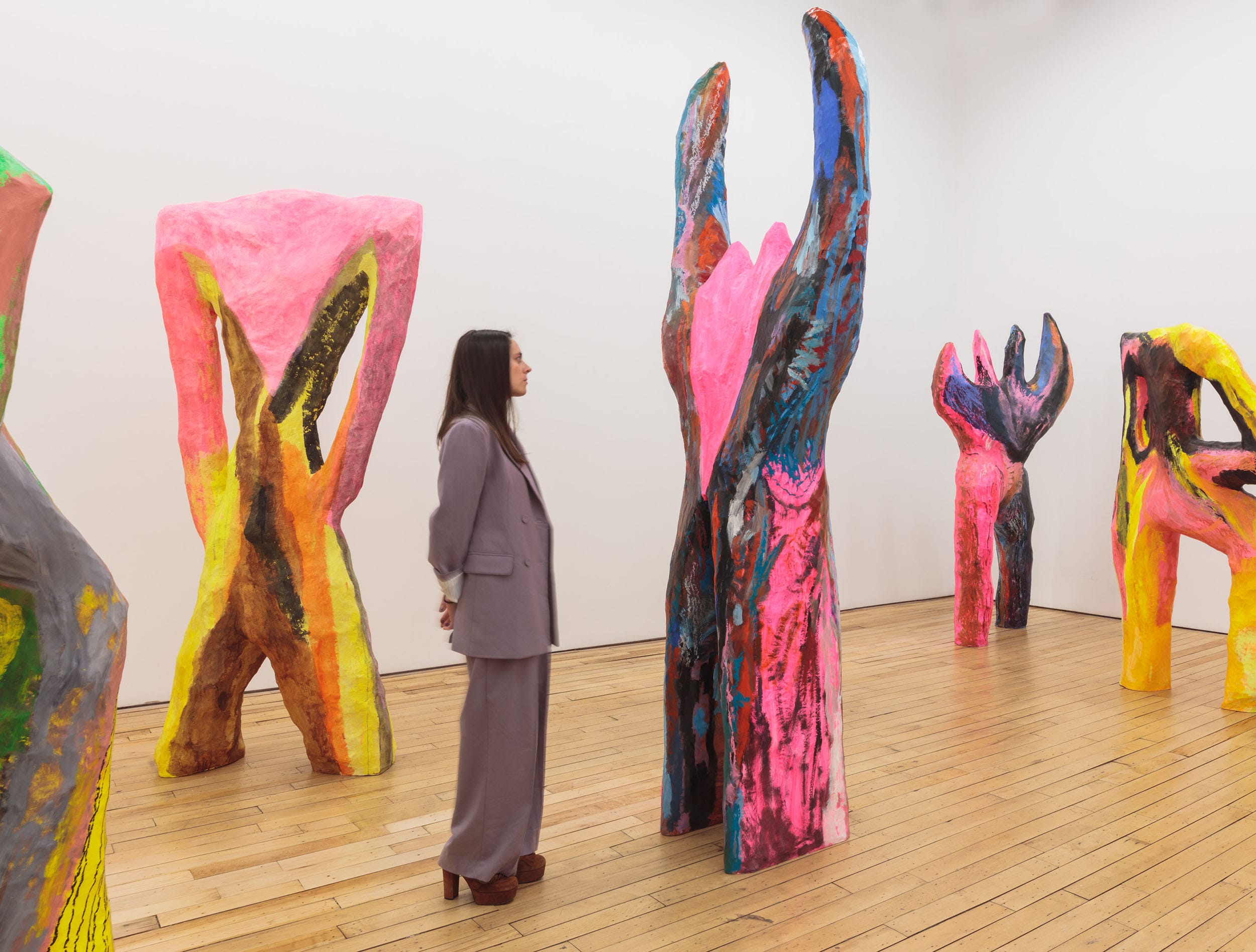 Woman in a gallery observing colorful, abstract sculptures on a wooden floor.