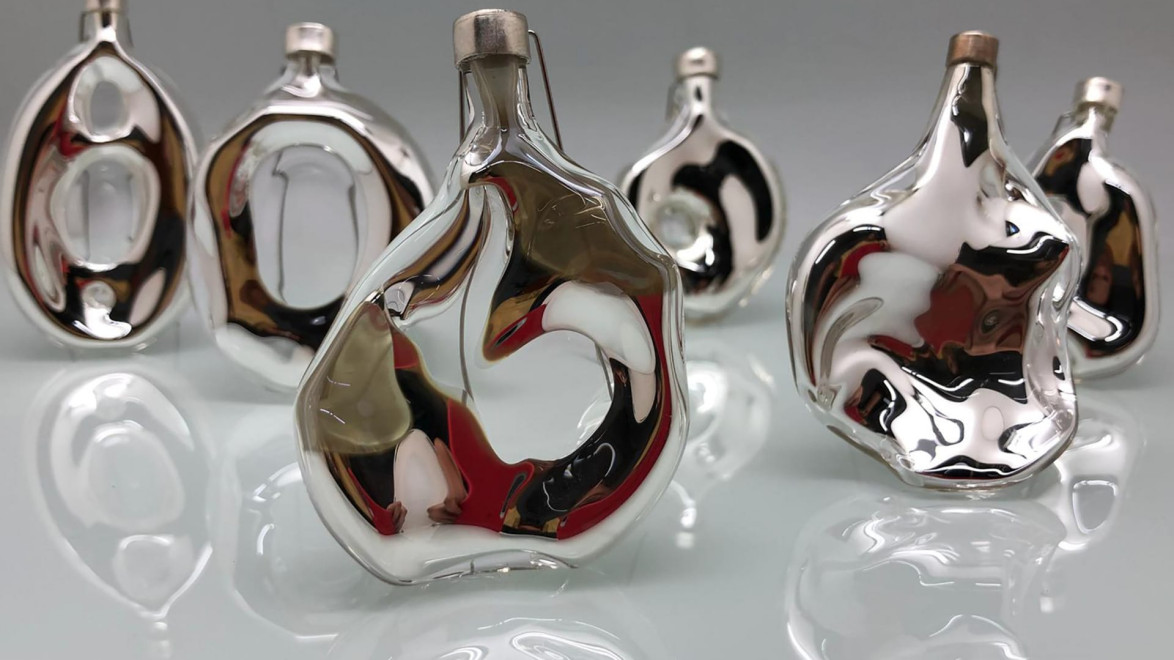 Abstract mirrored sculptures with fluid, reflective surfaces placed on a sleek, glossy white background.