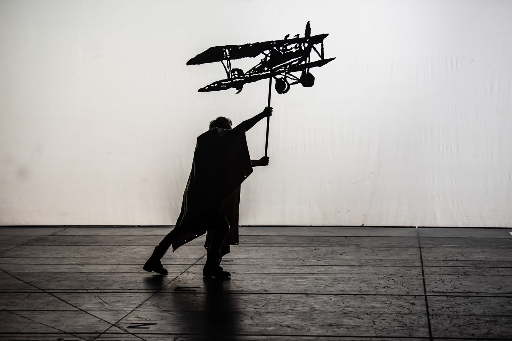 Silhouette of a person holding a large airplane model on stage against a plain white background.