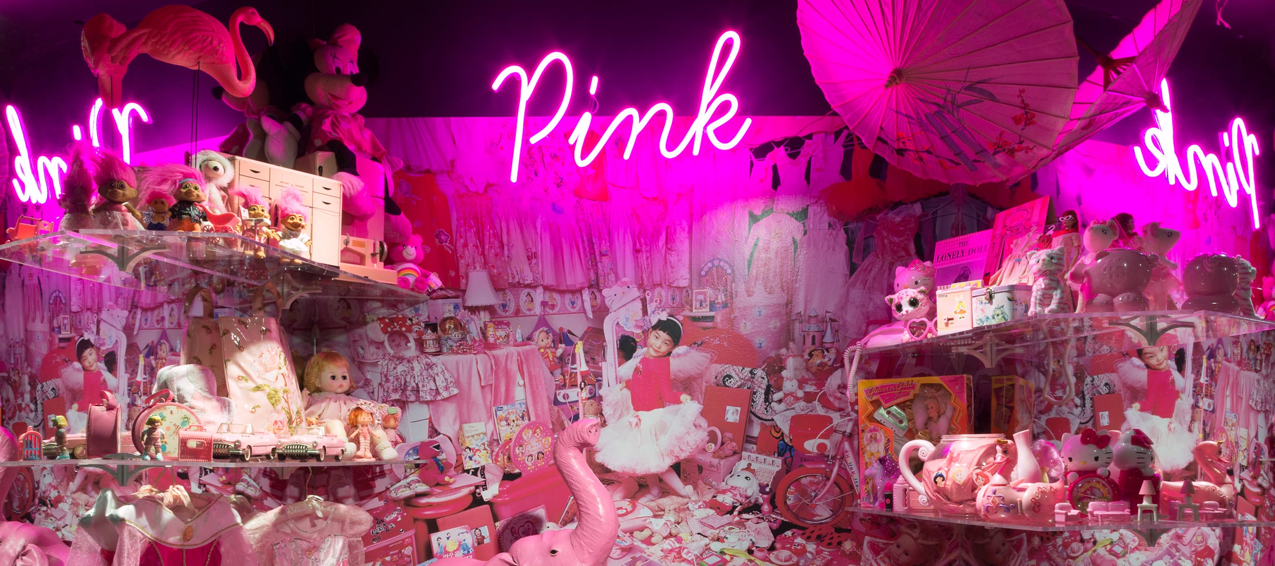 A vibrant display of pink toys and decor with a neon sign reading "Pink" above, featuring dolls, plushies, and accessories.
