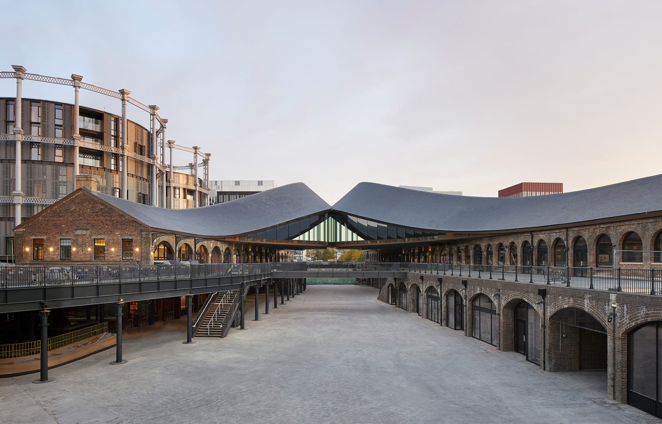 Modern architectural building with curved roofs, arched windows, and brick walls set in a spacious open courtyard.
