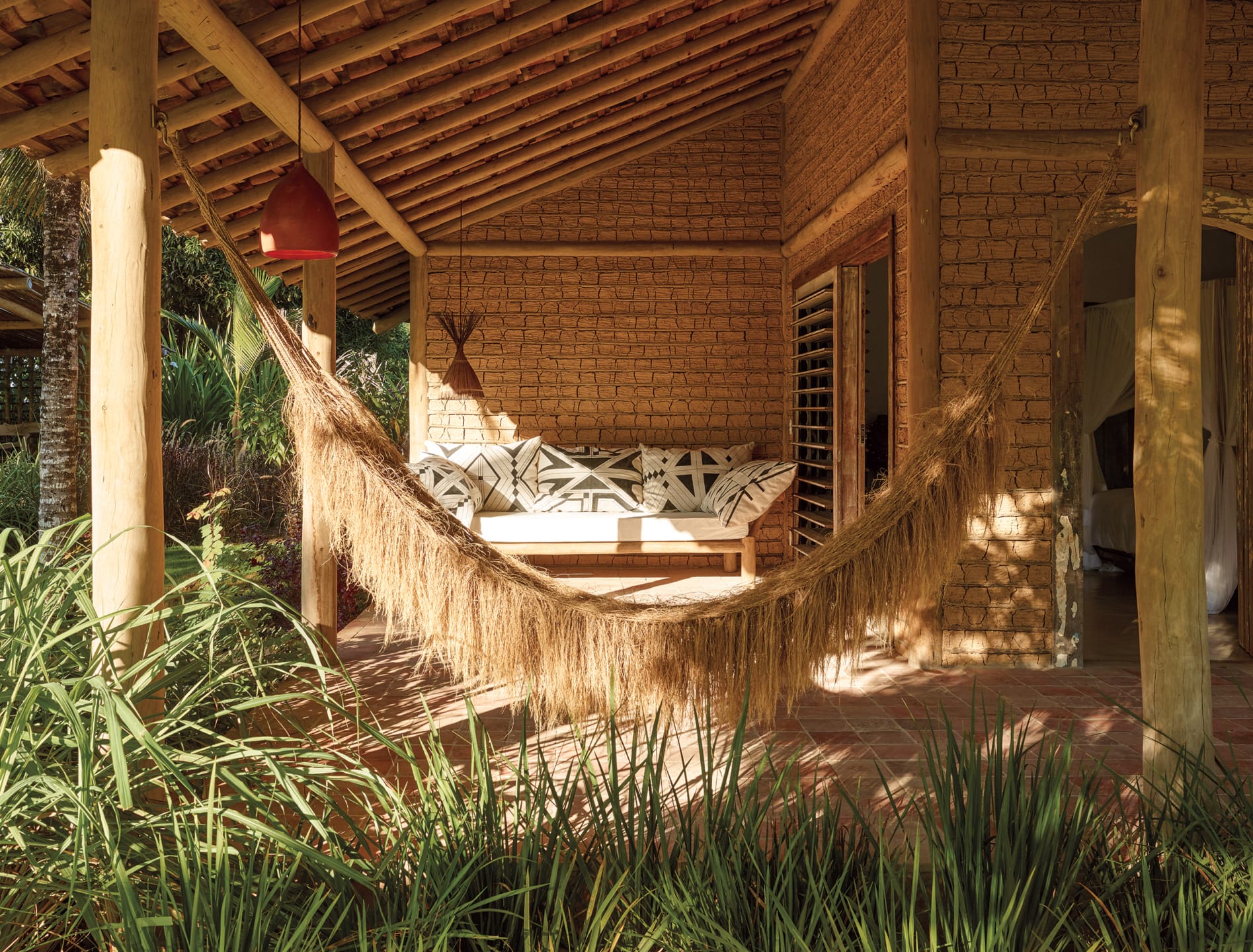 Cozy porch with a rustic hammock and cushioned seating, surrounded by lush greenery and wooden architecture.