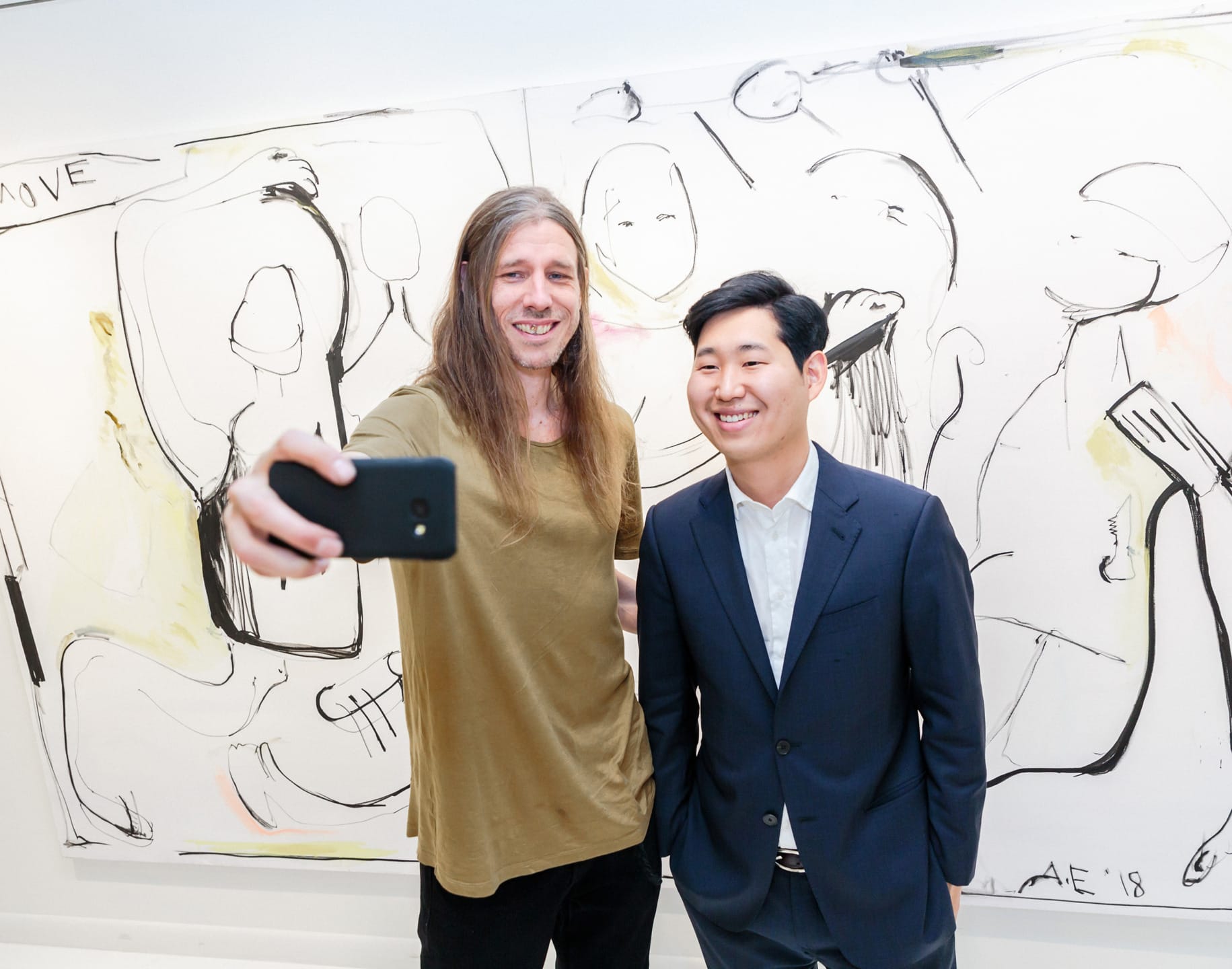Two people taking a selfie in front of an abstract art painting in a gallery setting.