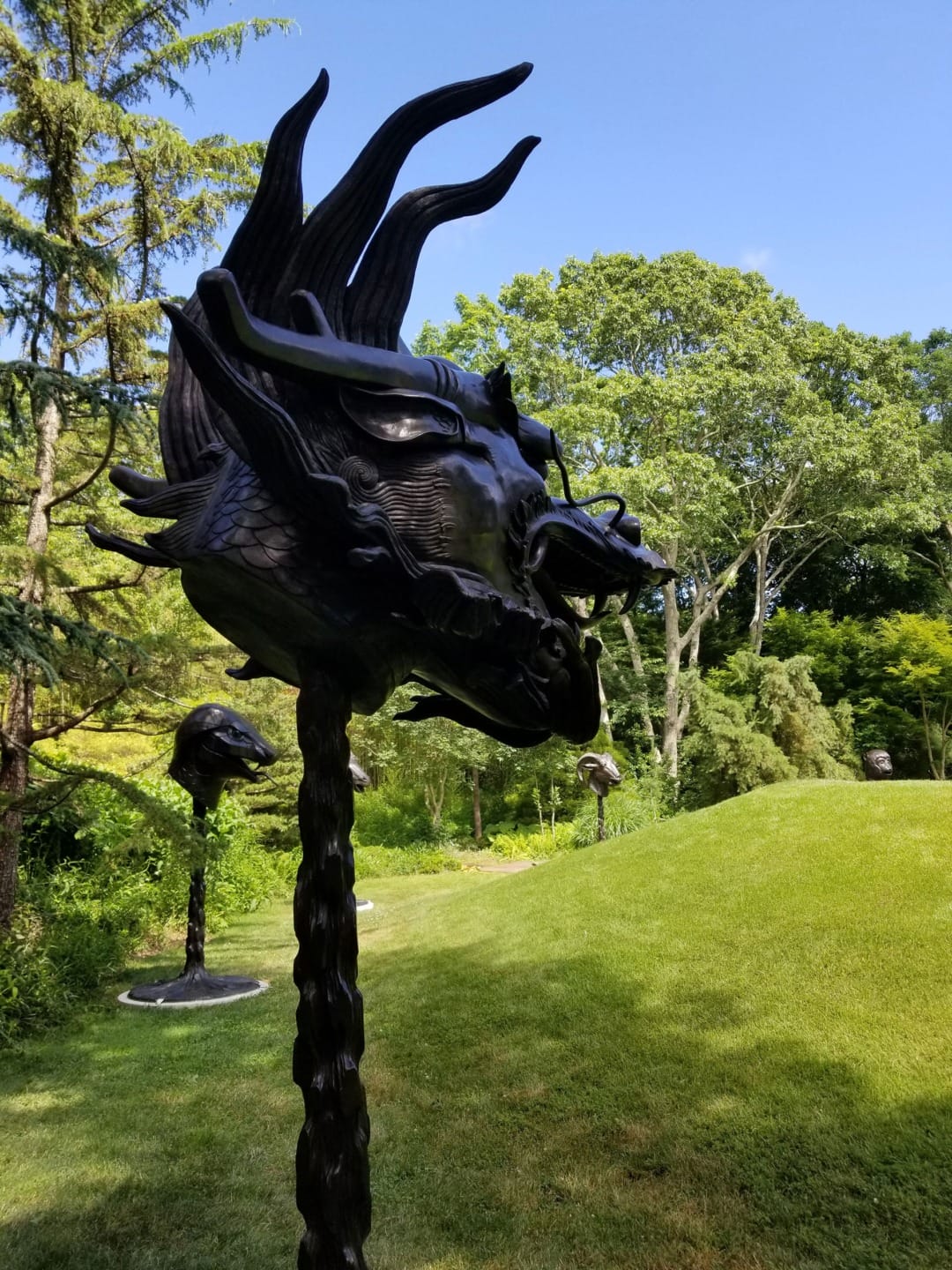 Sculpture of a dragon head outdoors on a sunny day with trees and grass in the background.