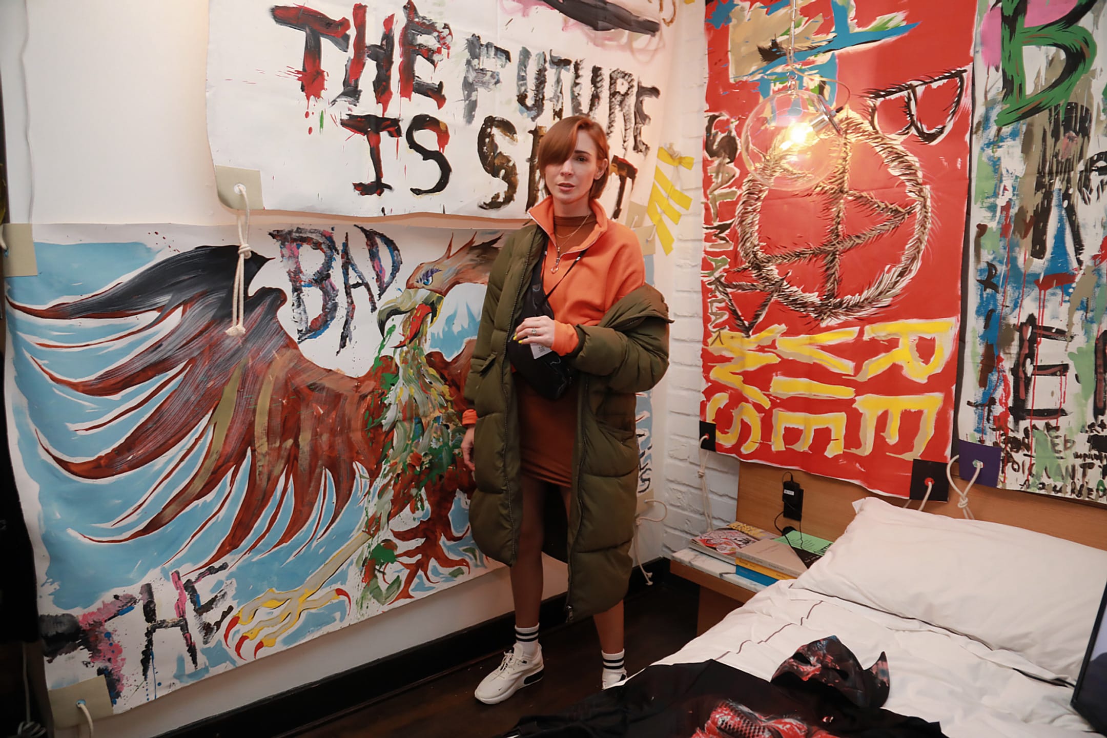 Person standing in a room with colorful graffiti-covered walls featuring various bold designs and a bed nearby.
