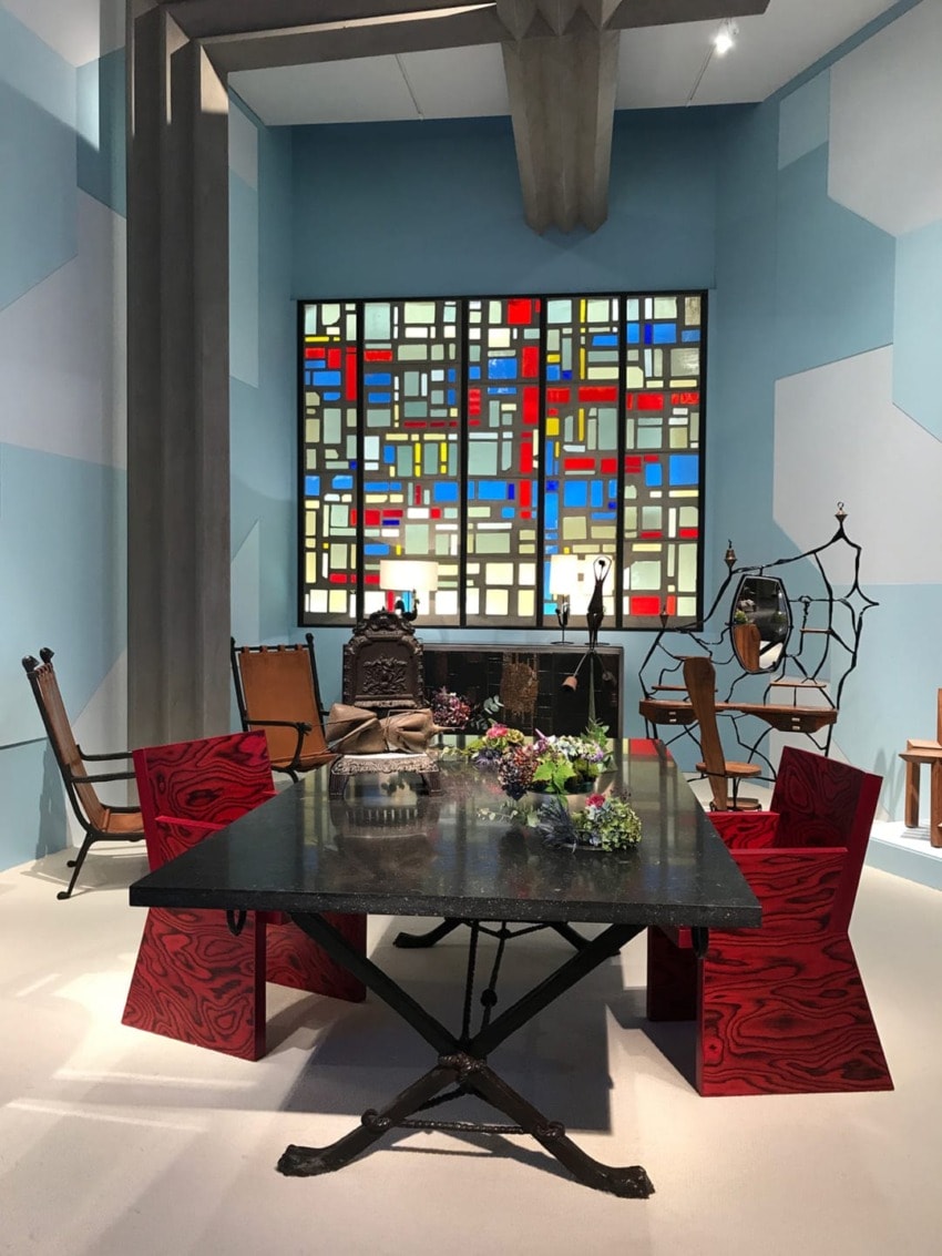 Modern dining room with artistic stained glass window, red and black chairs, and a table adorned with decorative elements.