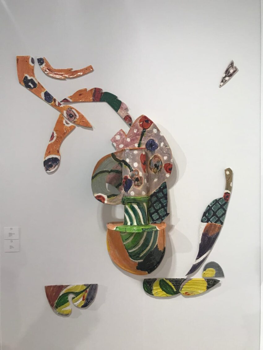 Colorful abstract wall sculpture with fragmented ceramic pieces and bold patterns on a white background.