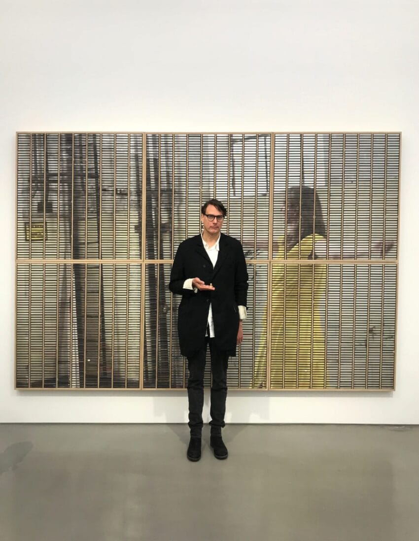 Person standing in front of abstract artwork with reflective silver and gold panels in a bright gallery space.