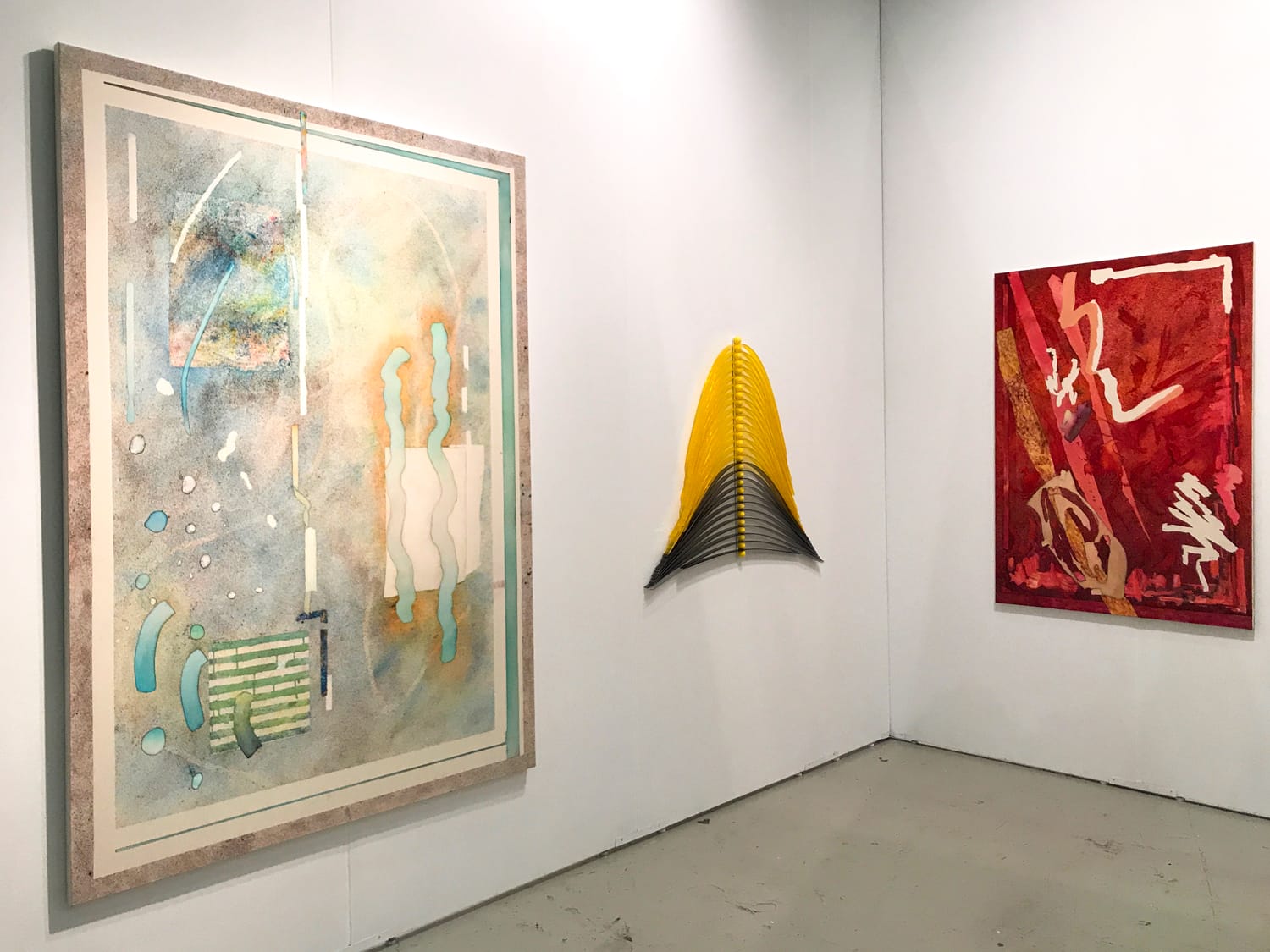 Contemporary art gallery with abstract paintings and a yellow and black wall sculpture on display.