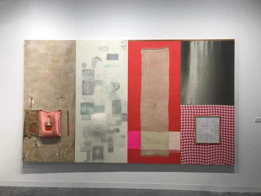 Abstract artwork with various textures and colors, including reds, pinks, and grays, displayed on a gallery wall.