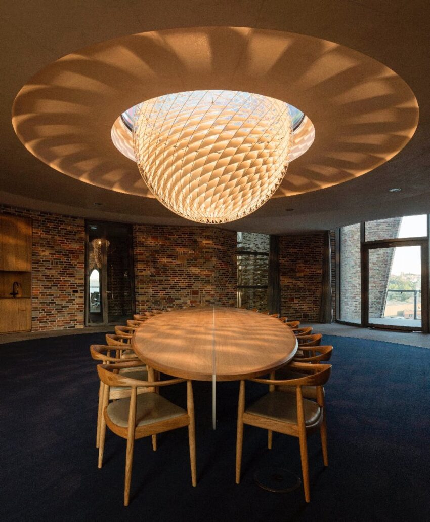 Modern dining room with a large round table, wooden chairs, and an intricate illuminated ceiling design.