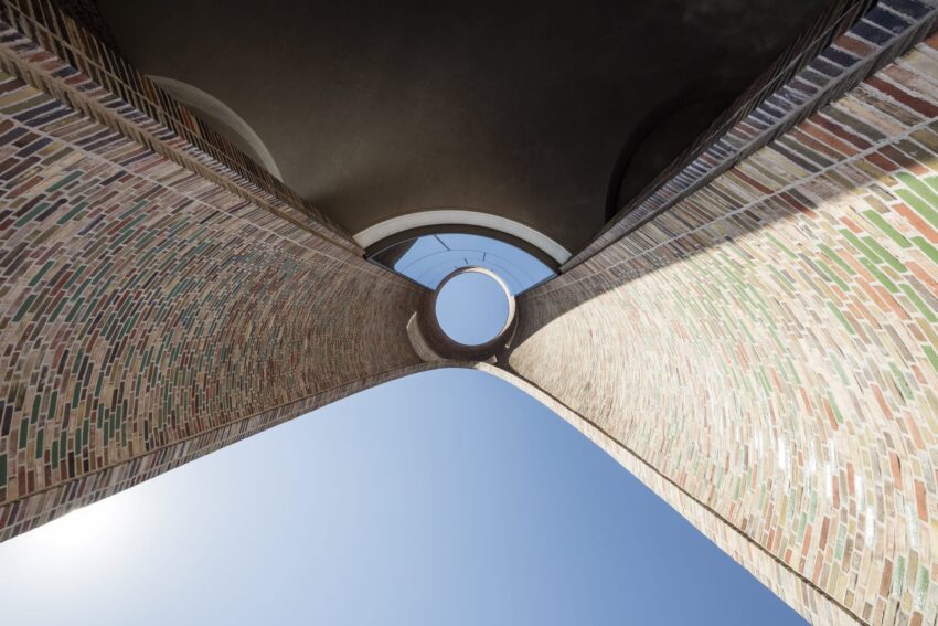 View of modern brick tower with circular opening and blue sky background.