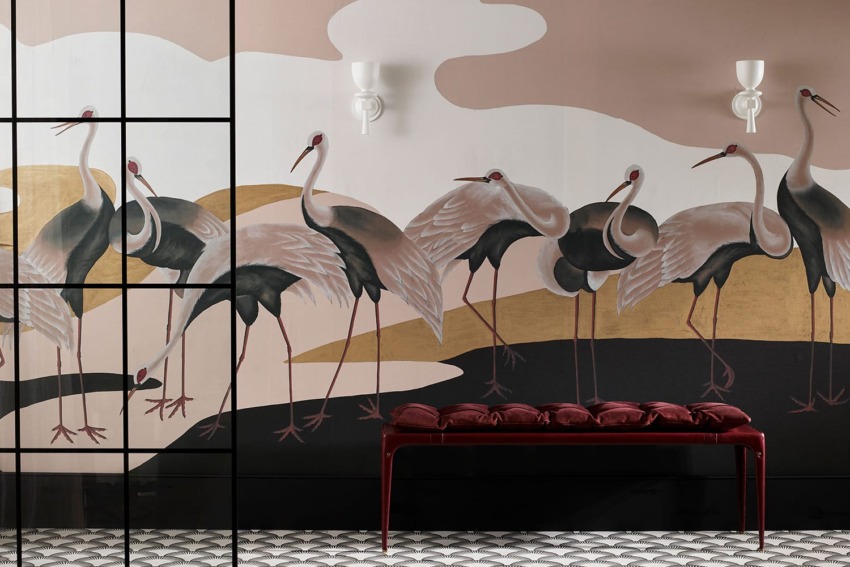 Wall mural featuring elegant cranes with stylized design, black and white floor tiles, and a red cushioned bench.