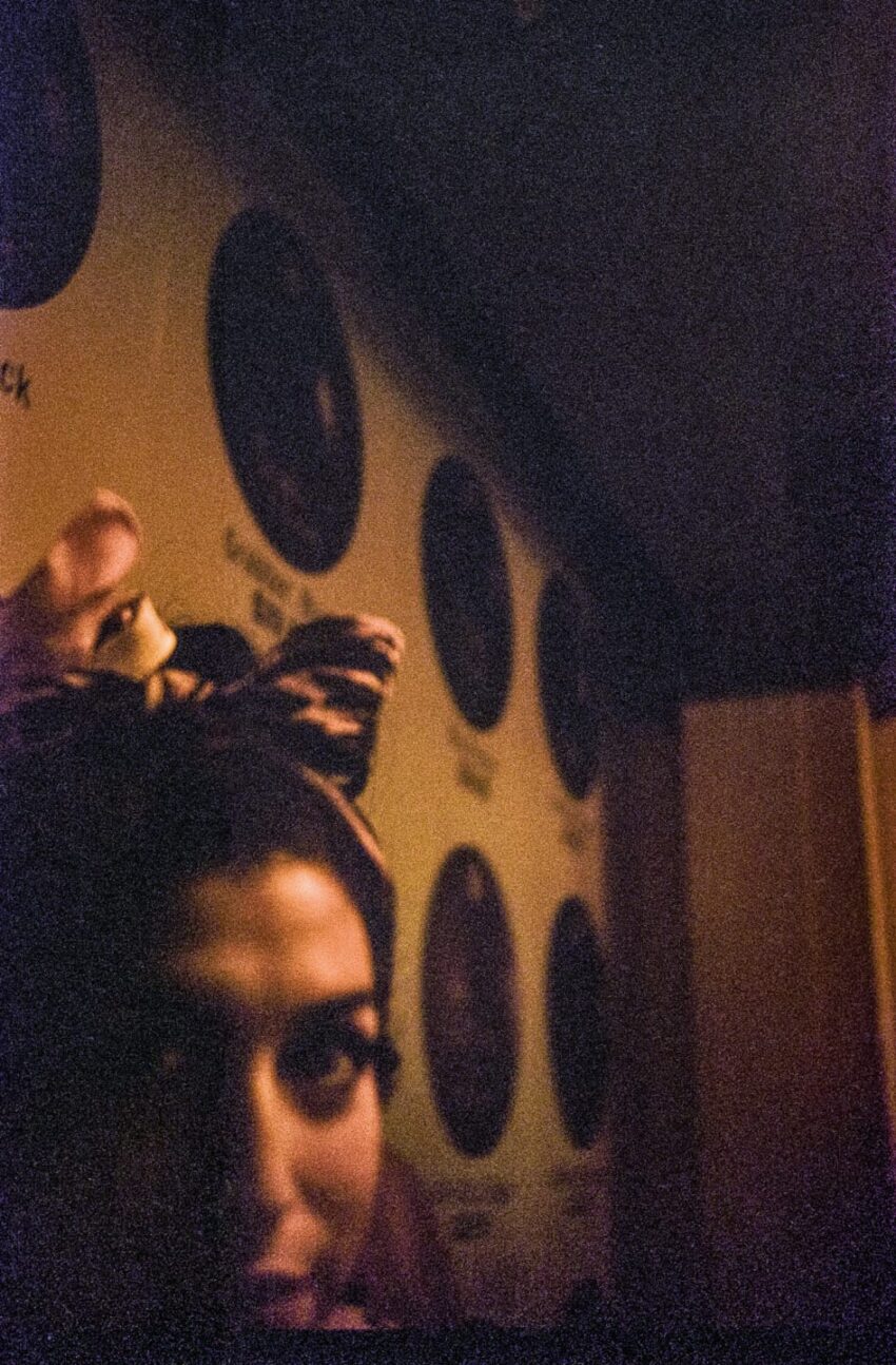 Person partially visible in dim lighting, wearing leopard ears headband, with circular wall decorations in the background.