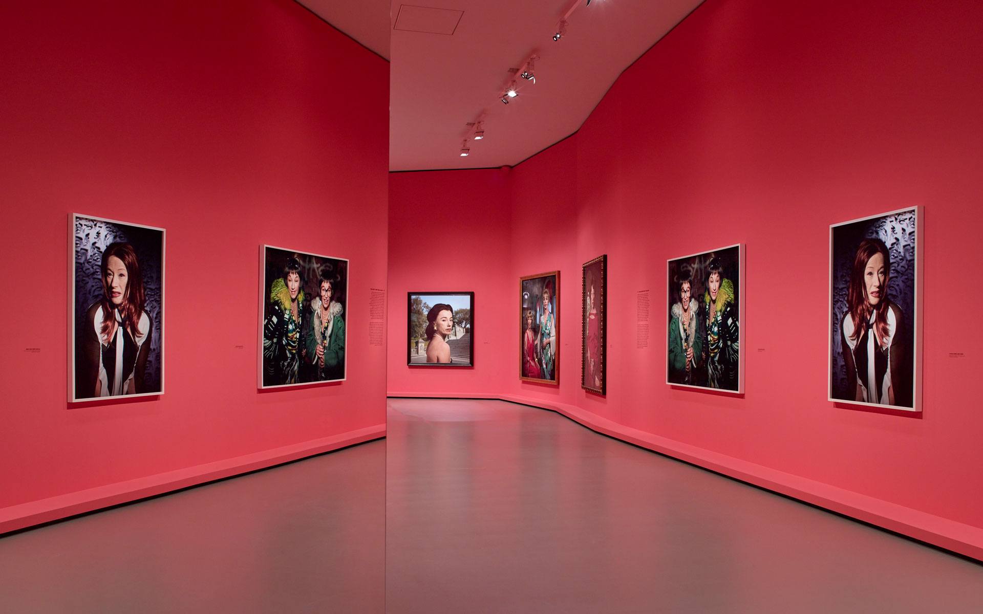 Art gallery with bright red walls displaying various portrait photographs in elegant frames.