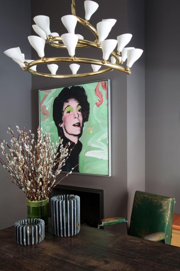 Artistic dining room with modern chandelier, abstract portrait artwork, green chair, vases, and pussy willow branches.