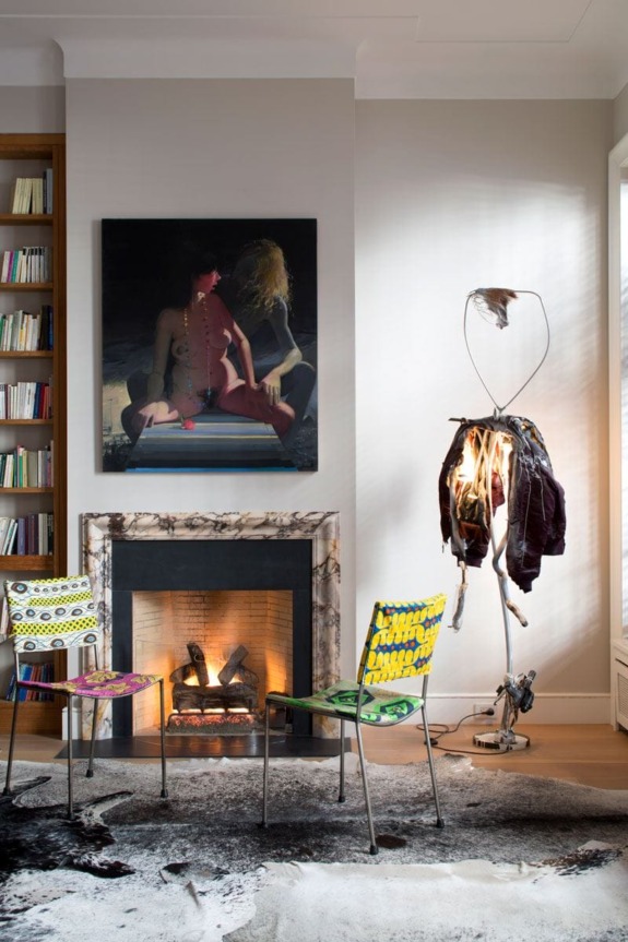 Modern living room with abstract art, colorful chairs, a unique lamp, and a fireplace for a cozy, eclectic vibe.