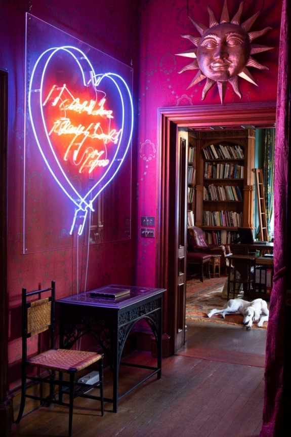Colorful room with neon heart sign, ornate decor, wooden desk, and a dog lying in the library doorway.